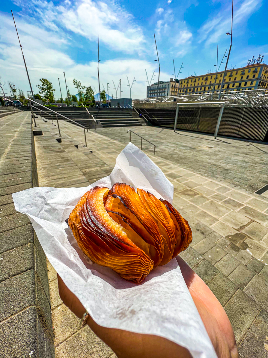 Image of Shireen's left palm holding a Sfogitalle on a white napkin in front of Naples Central Station in Naples Italy