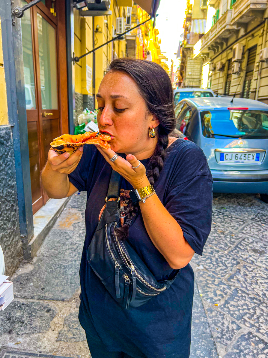 Image of Shireen eating a slice of margarita pizza outside Michele da Pizzeria in Naples Italy