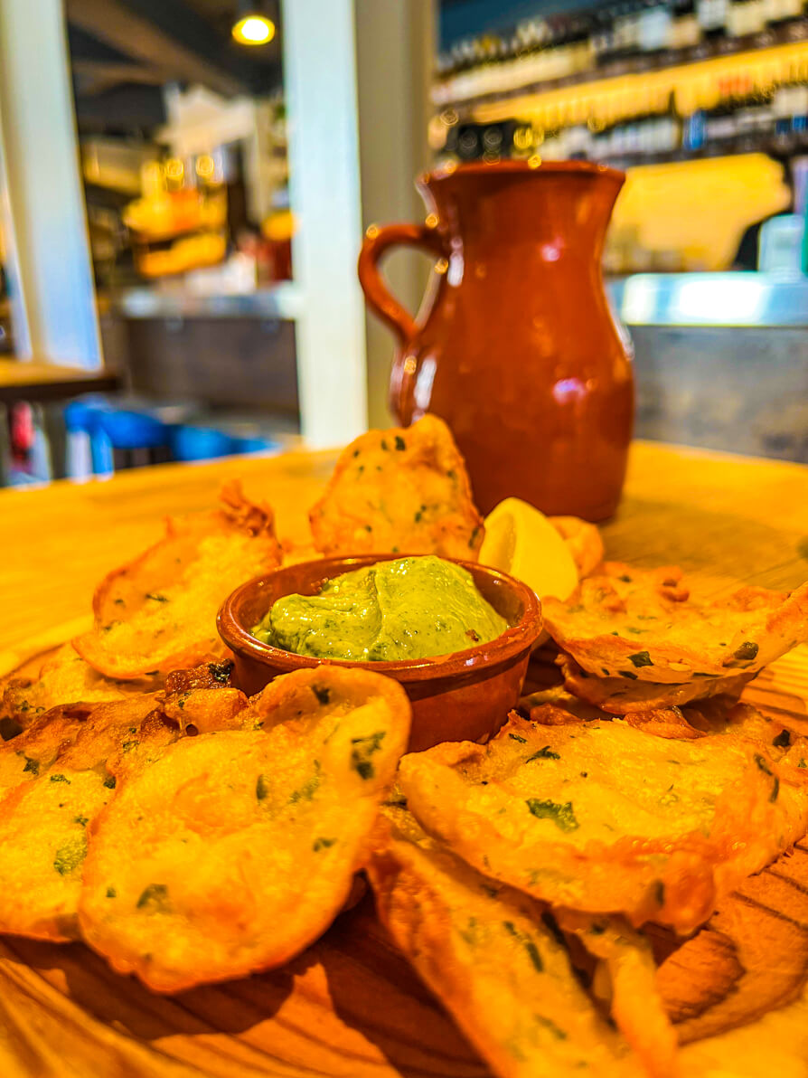Image of prawn tortilla fritters up close with green dip in centre with brown jug in background in Curado Cardiff