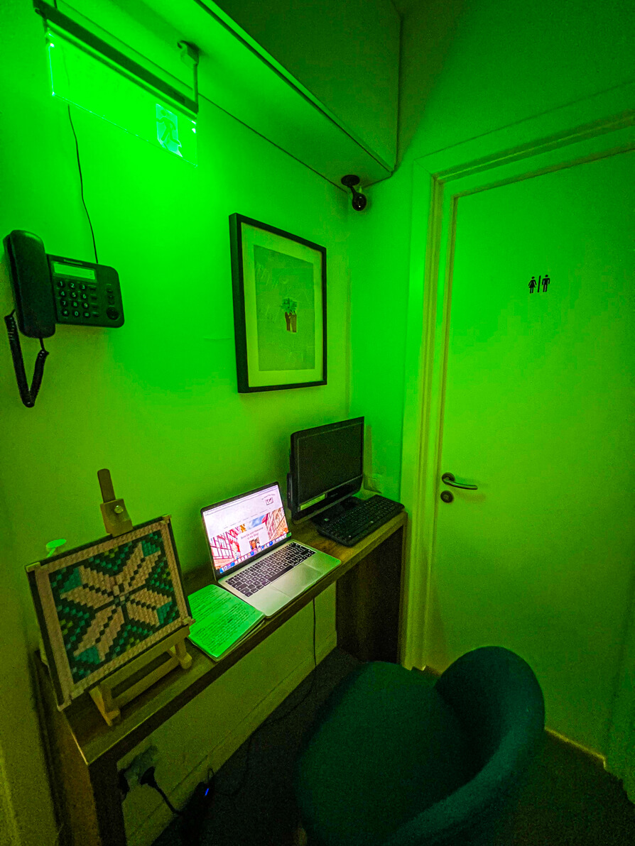 Image of public space in First Hostel with desk and computer on top, chair, phone and decor on wall.