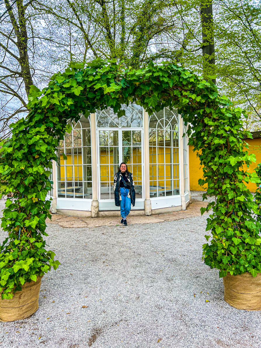 Image of Shireen posing in front of the gazebo at Hellbrunn Palace with arch of flowers overhead in Salzburg Austria