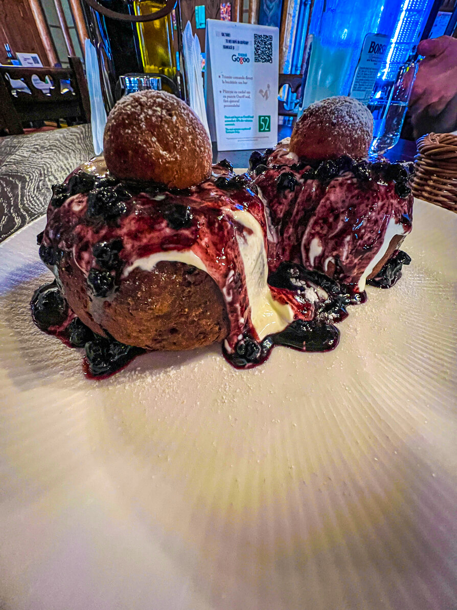 Image of two papanasi on white plate with blueberry jam in Bucharest Romania