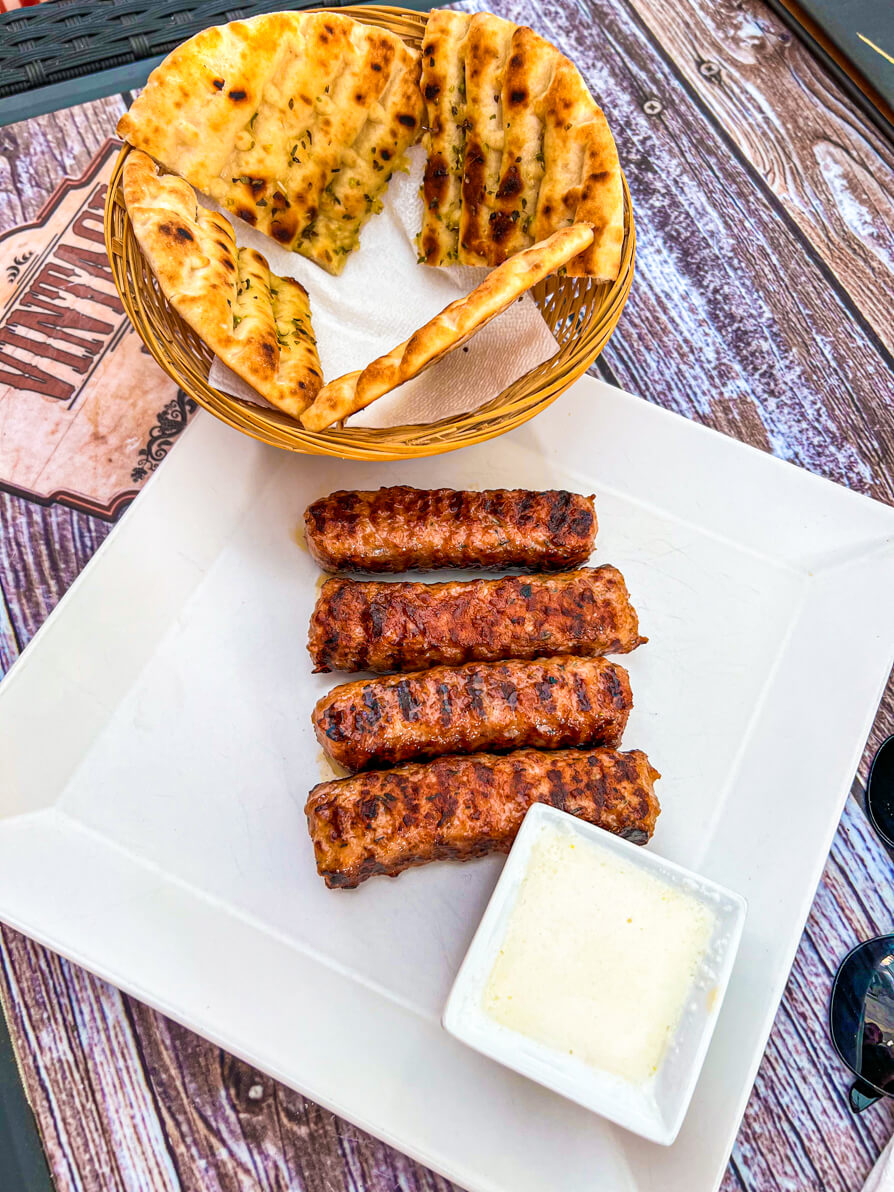 Image of 4 mici on a white plate with white bowl of garlic sauce in Romania