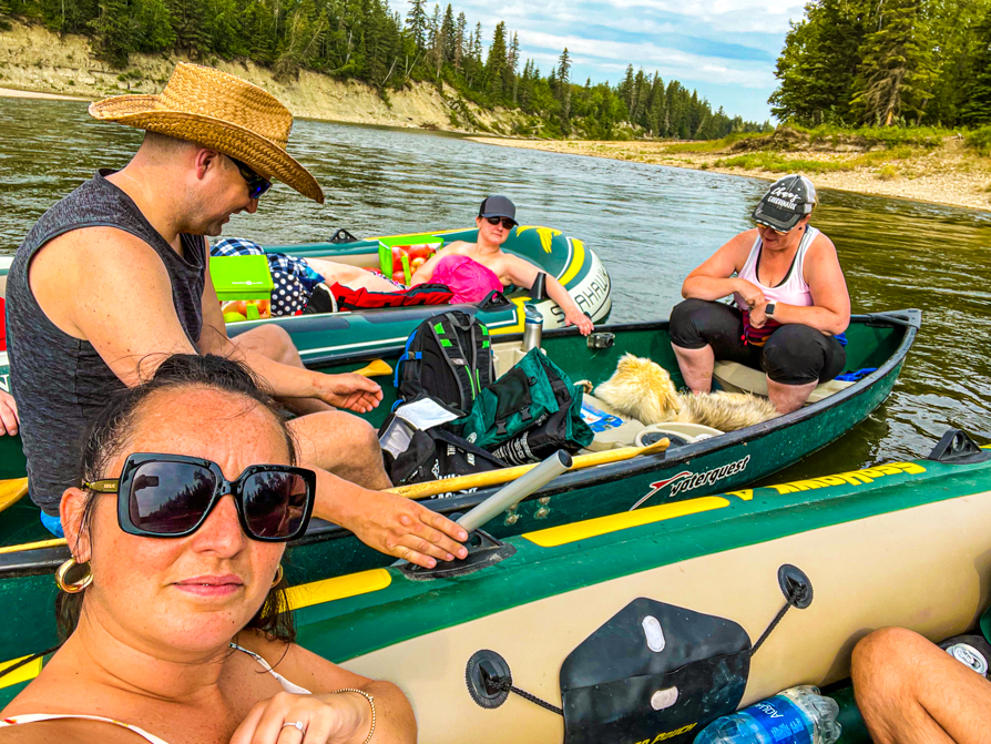 Image of Shireen taking a selfie with three boats and canoe tied together on Red Deer River while floating