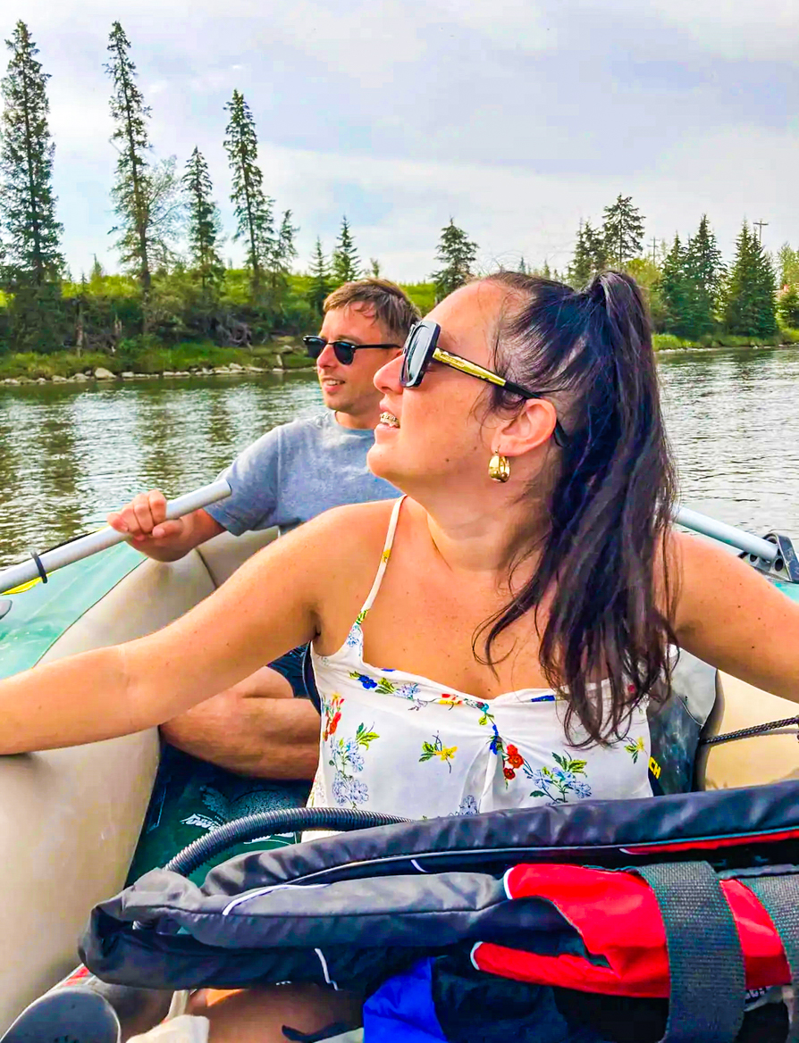 Image of Shireen and Scott looking to the left while canoeing Red Deer River with river in back and both sat on inflatable boat in Alberta Canada