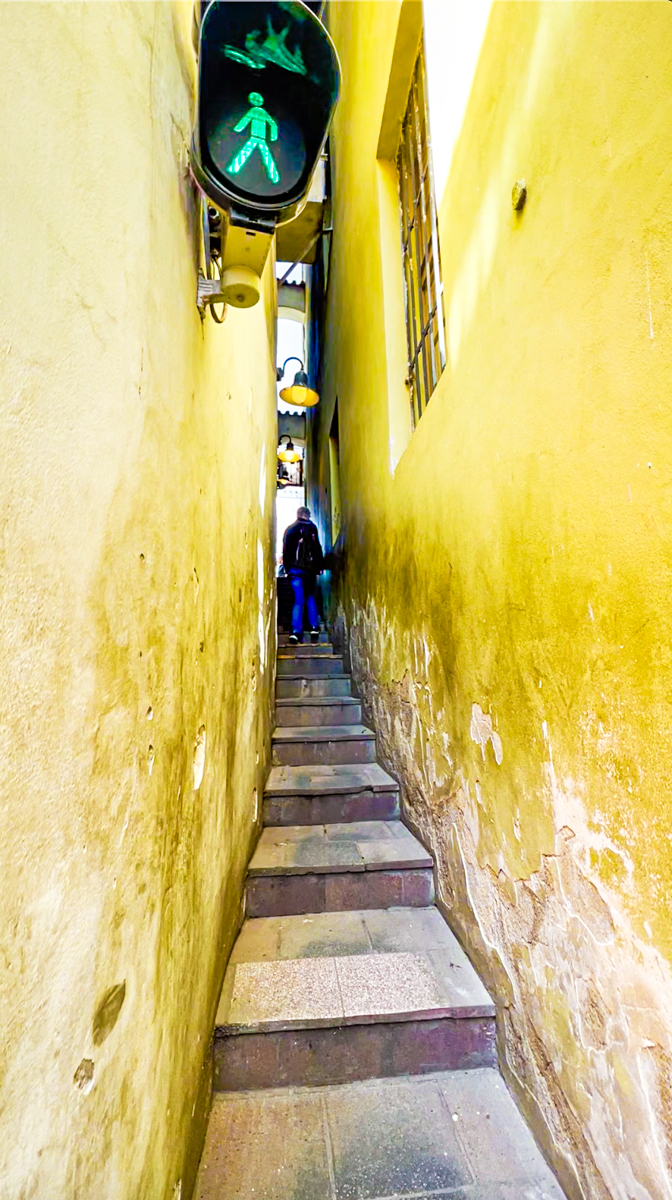 Image of the  most narrow street in Prague between yellow walls and green traffic light in top left corner