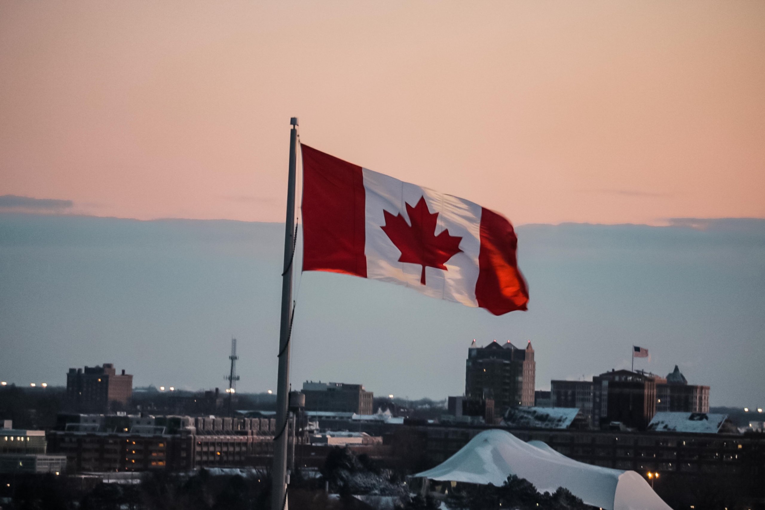 Image of Canadian flag flying with pink sky and city line in background