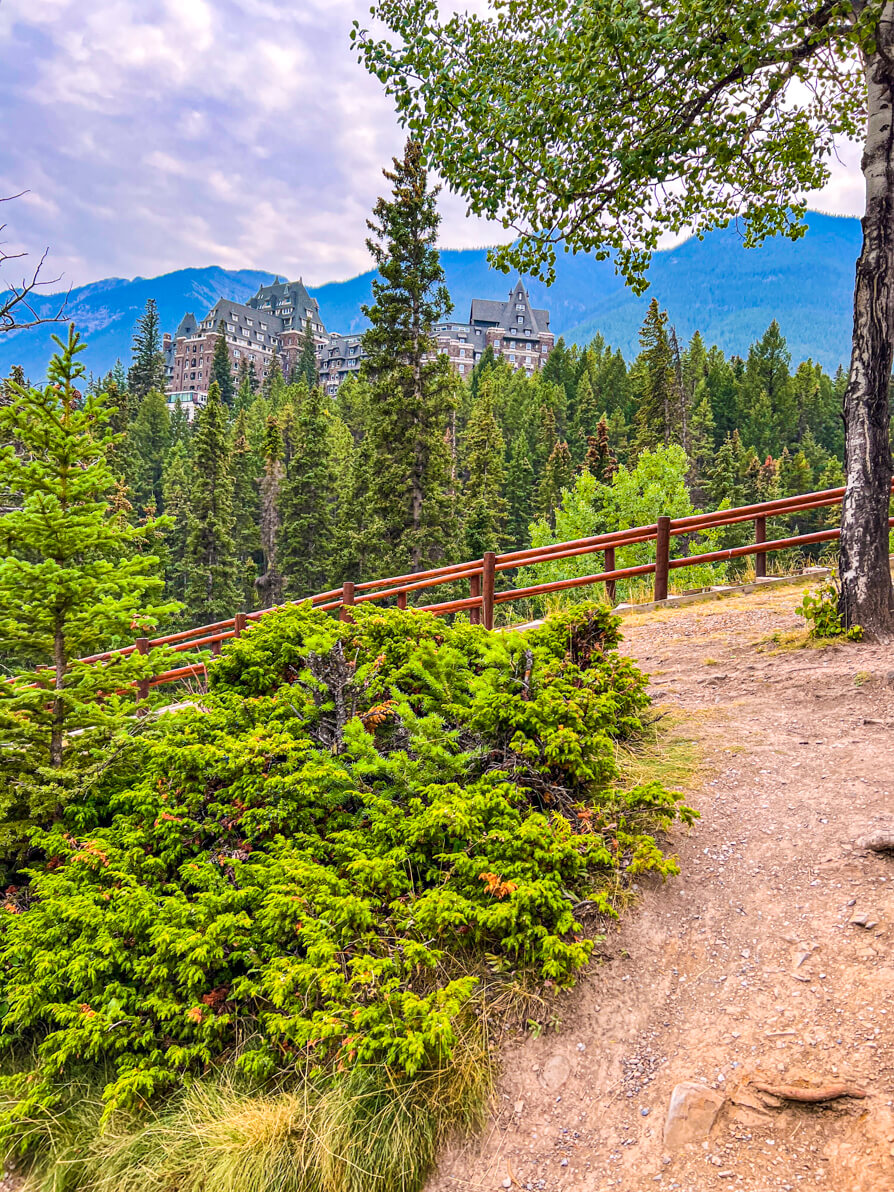 Image of path and bushes on Bow Falls trail with trees and Banff Springs Hotel in background in Banff Canada