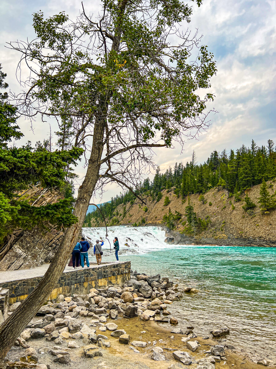 wide shot image of bow falls, river and people posing at the photo spot in Banff Canada