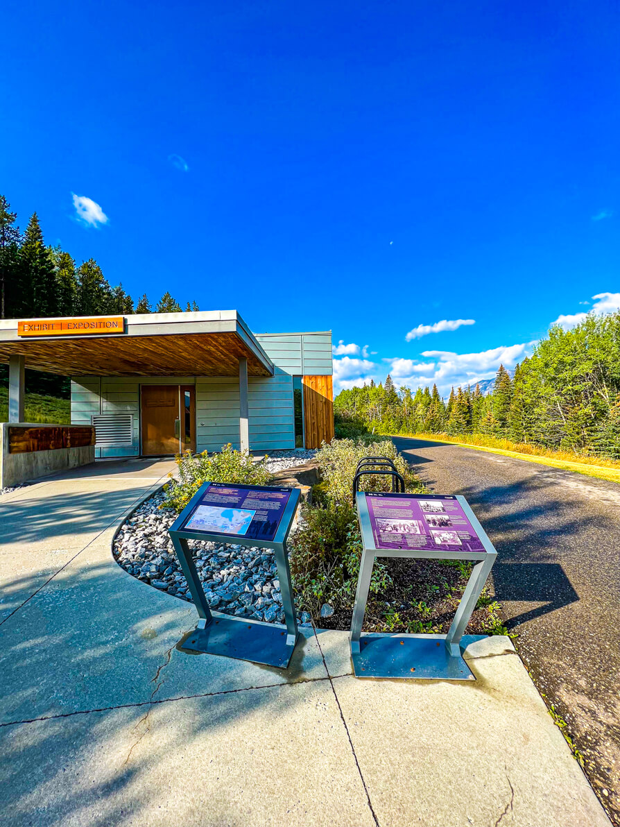image of exhibit exposition building on the Marsh Loop trail sign on green post outside cave and basin in Banff