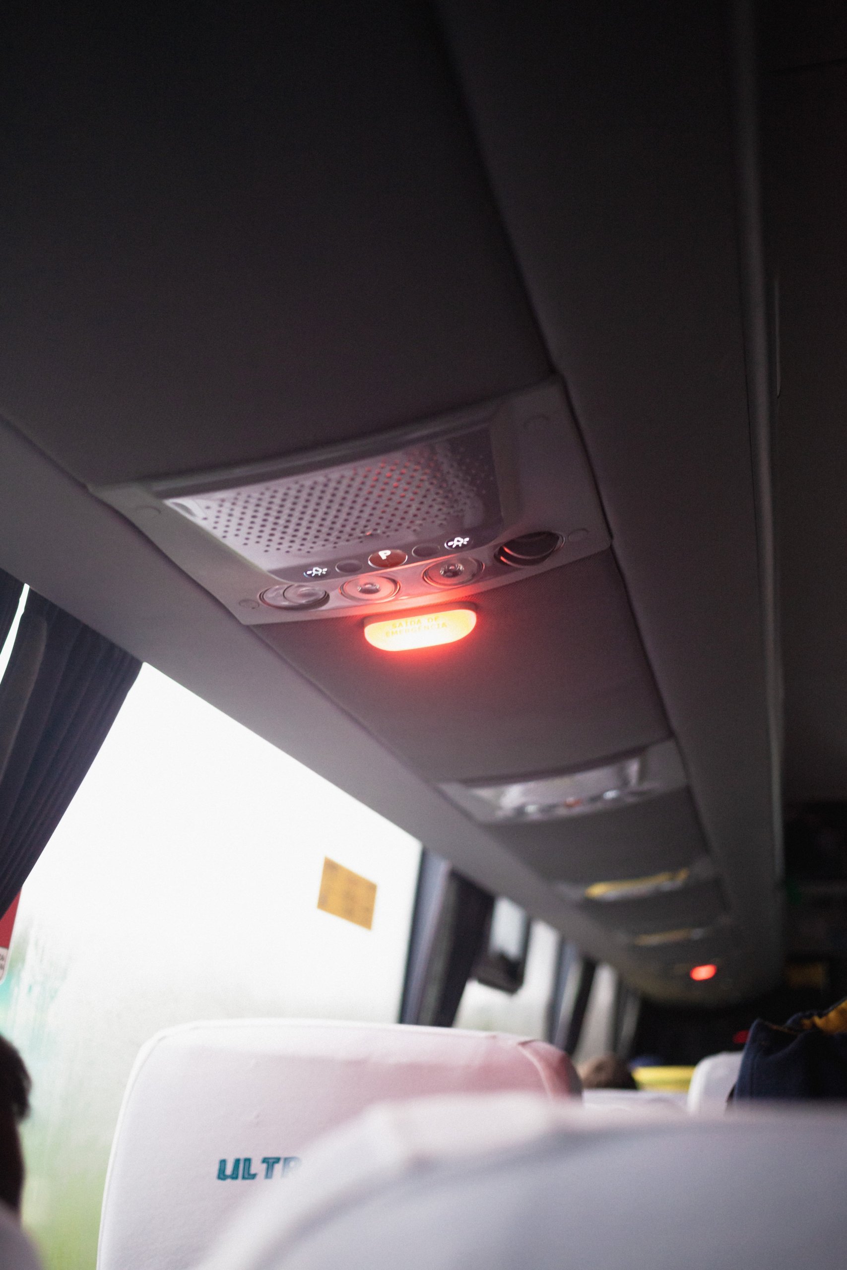 Image of bus interior of the back of a chair, air conditioning on top and side window