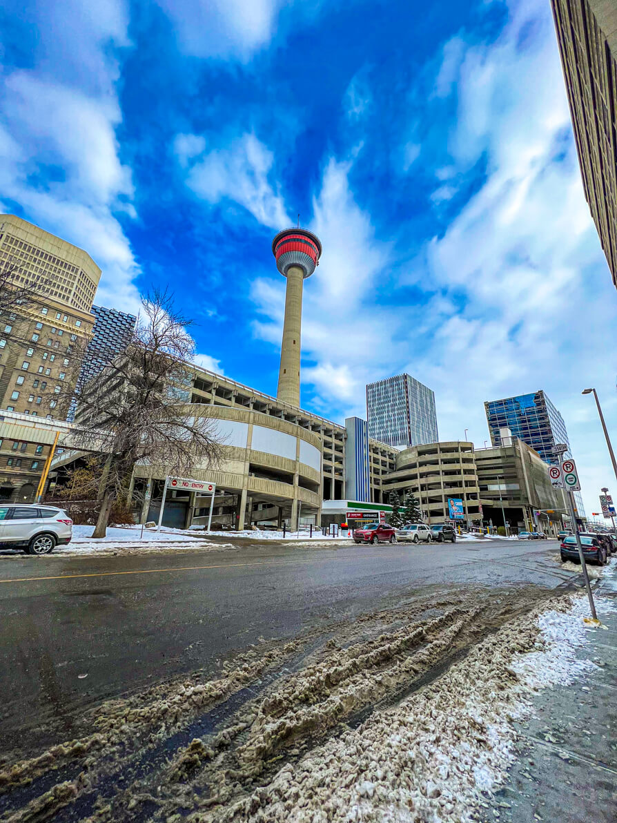 Image of calgary tower from street view. Wide shot is looking up at the tower with blue sky behind.