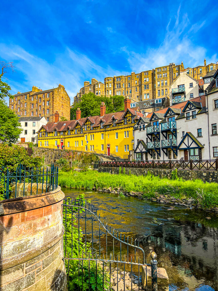 image of Dean Village Edinburgh. Yellow and white houses in a row in centre, leith river in front and blue sky in back