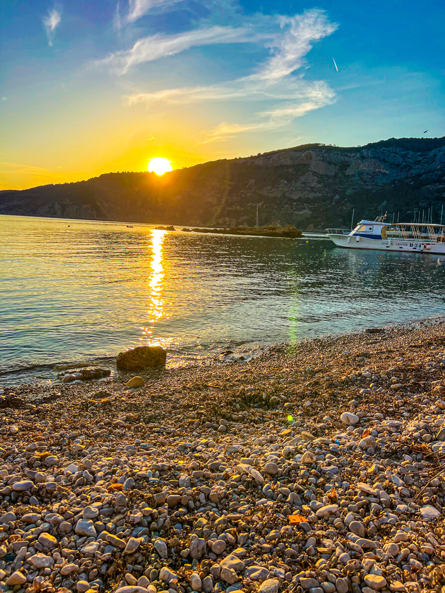 image of Vis island beach with stones in front, sea in centre, mountains in background with sun setting