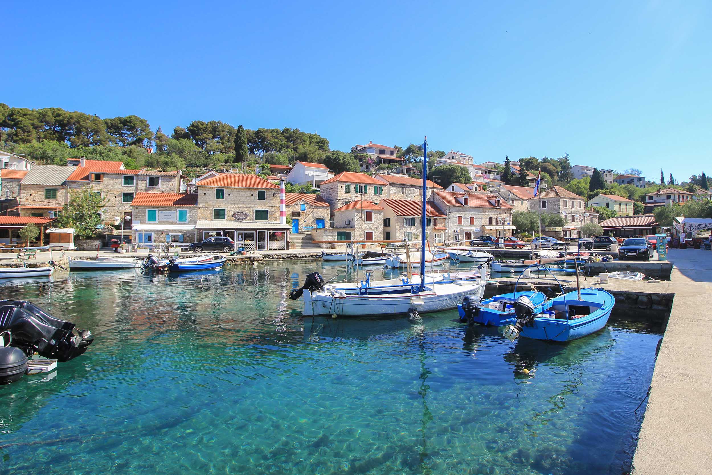 image credit to placesofjuma. Image of Solta Island harbour with boats, houses and water with blue sky behind