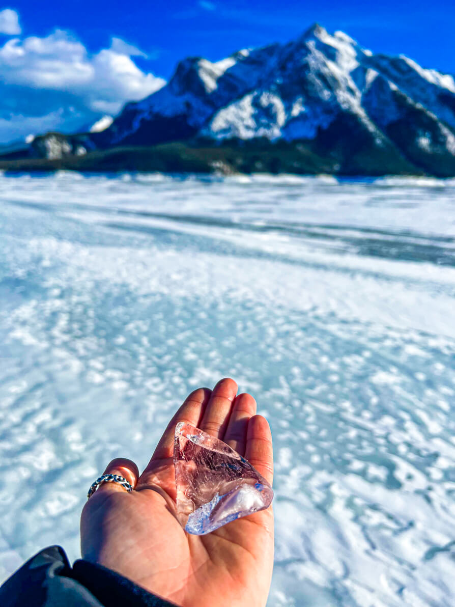 Shireen's left hand holding an ice block infront of Mountain at Lake Abraham