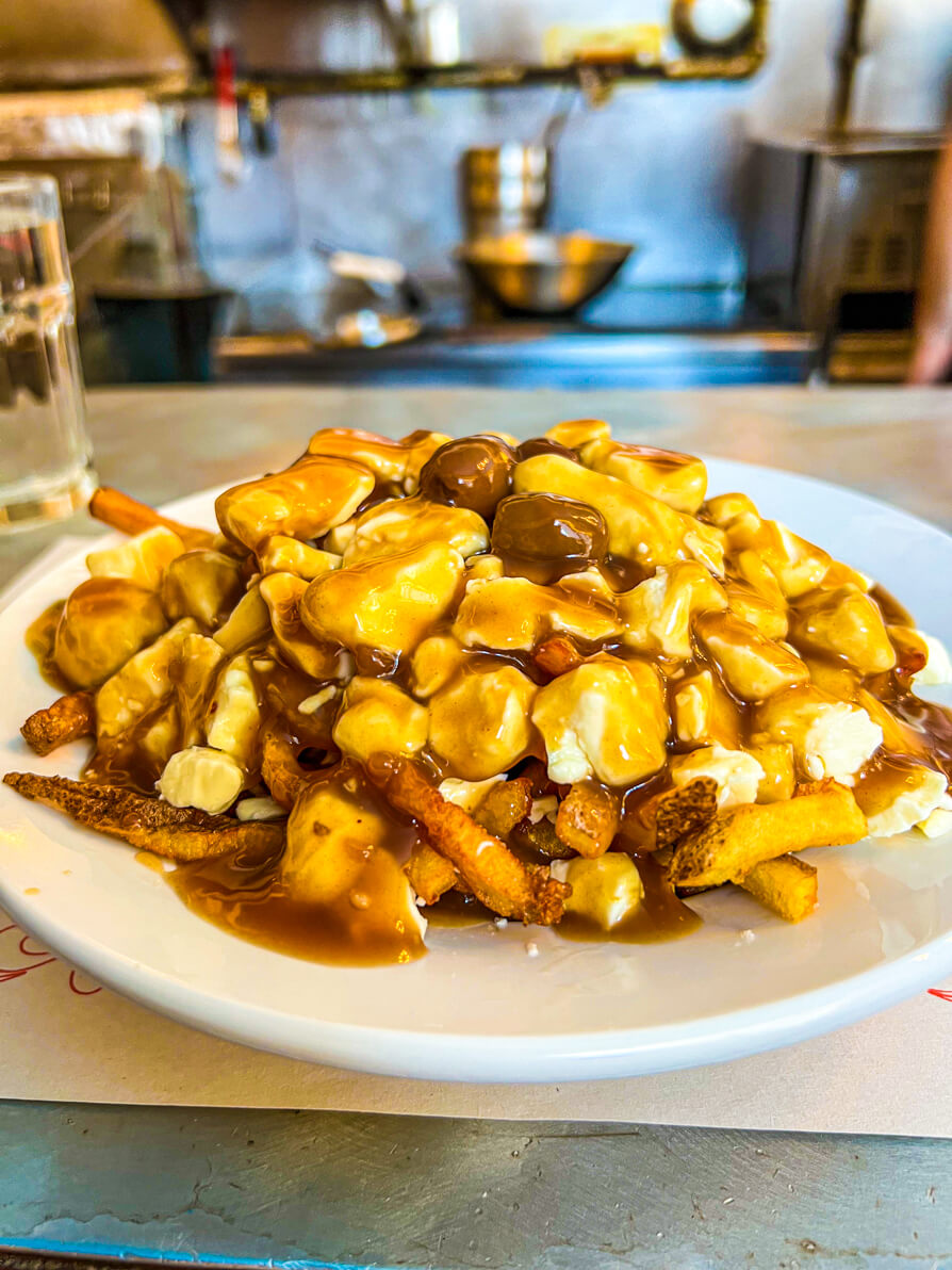 IMAGE OF CLASSIC POUTINE IN MONTREAL. POUTINE ON A WHITE PLATE ON THE BAR OF A POUTINERY IN MONTREAL CANADA AS PART OF MONTREAL FOOD TOUR