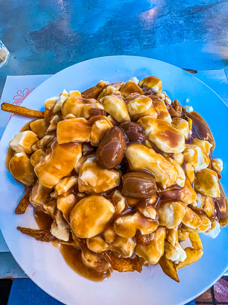 IMAGE OF CLASSIC POUTINE IN MONTREAL. POUTINE ON A WHITE PLATE ON THE BAR OF A POUTINERY IN MONTREAL CANADA AS PART OF MONTREAL FOOD TOUR