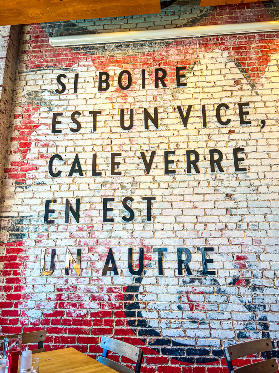 Image of writing on the wall at Si Boire. Text reads 'Si Boire Est Un Vice, Cale Verre En Est Un Autre' Roughly translates to 'If drinking is a vice then leaving half a glass is another'.