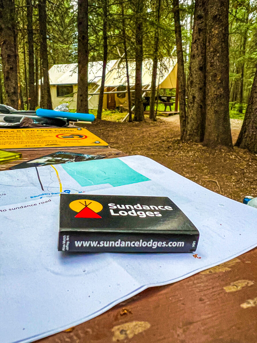 image of trappers tent in Sundance Lodge Kananaskis Country in background with souvenir matches in forefront of image reading 'Sundance Lodges' on the bench